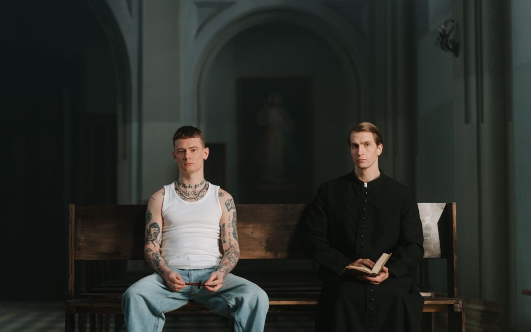 a tattooed man sitting beside a priest
